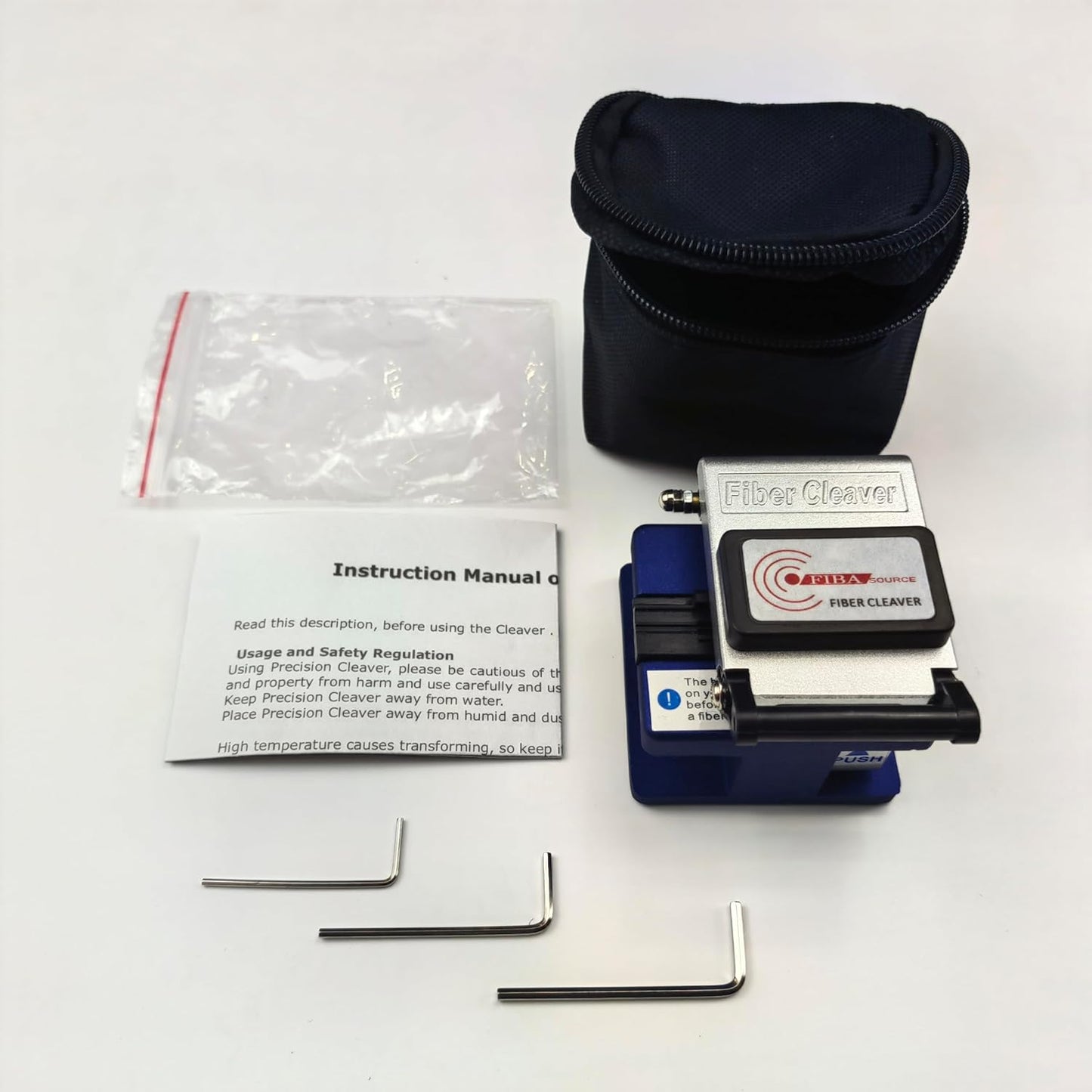 A Fibre Optic Cleaver from FIBAsource Ltd, featuring a branded logo, is elegantly displayed on a white surface. Alongside the cleaver are two L-shaped hex keys, a detailed instruction manual emphasizing precision cleaving methods, and a compact black zippered pouch for secure storage.