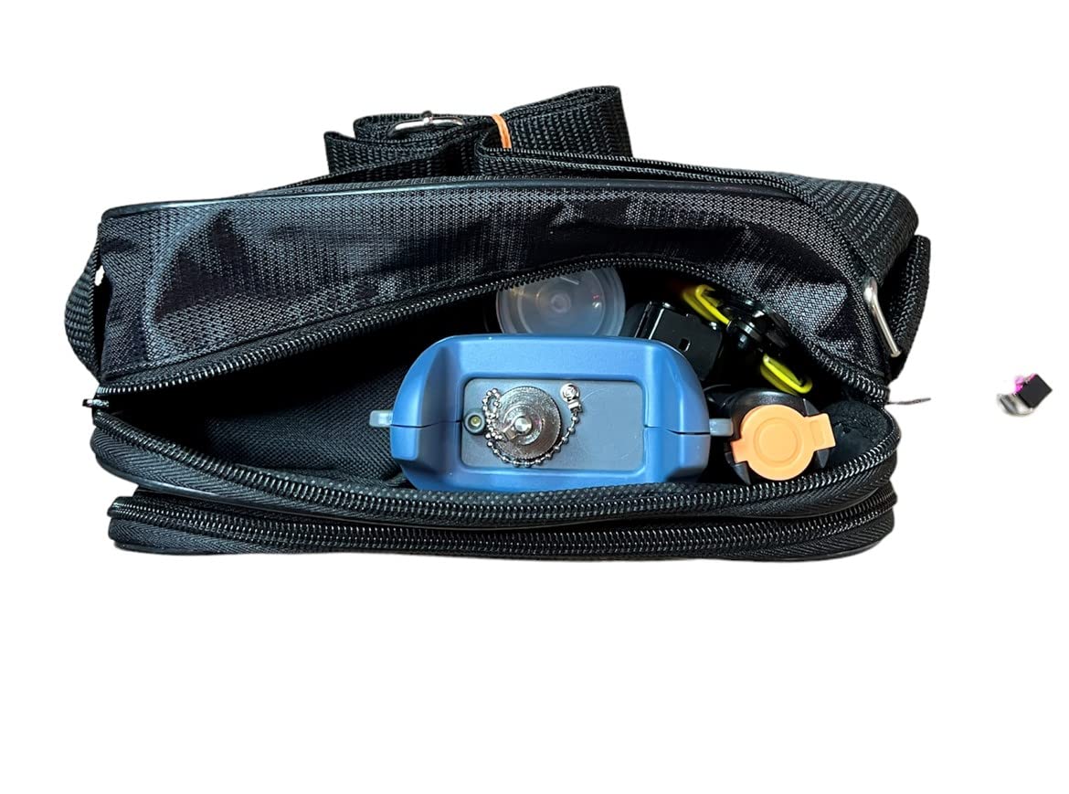 An open black travel bag reveals a blue camera, yellow-lensed glasses, and an orange bottle cap. A small black and purple object, part of the 9 in 1 Fibre Optic Tool Kit by FIBAsource Ltd, lies outside the bag on the right.
